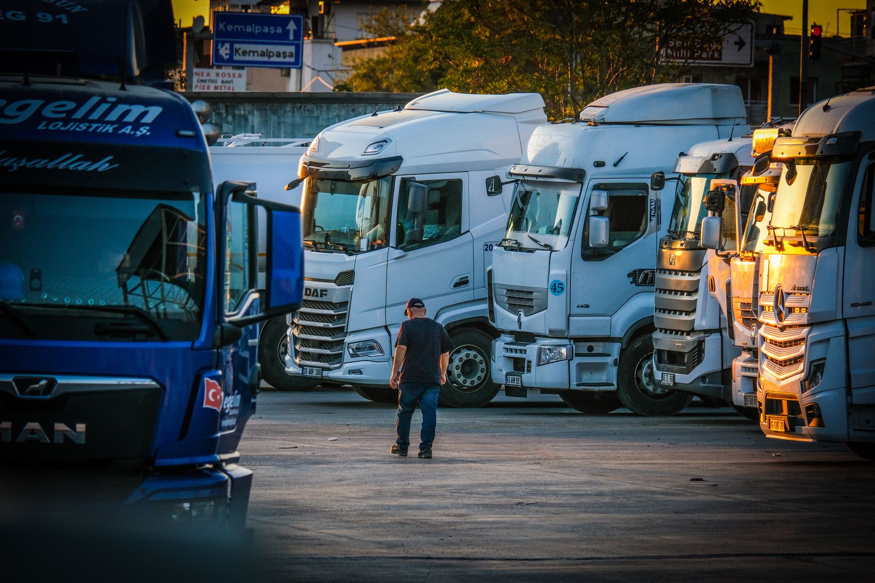 Trucks lined up at a depot at sunset while a dispatcher walks the yard